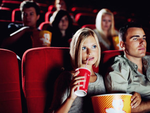 Caucasian couple watching suspenseful movie in theatre, woman drinking a soda with a straw