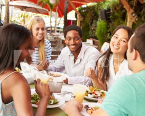 Group of friends of all ethnicities enjoying food and drinks on a patio