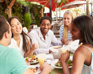 Group of friends of all ethnicities enjoying food and drinks on a patio