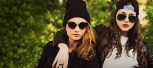 Two girlfriends in cool weather wear hanging out, one with her arm over the other's shoulder