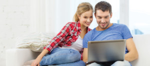 Young woman and man sitting together on a couch, looking at their laptop