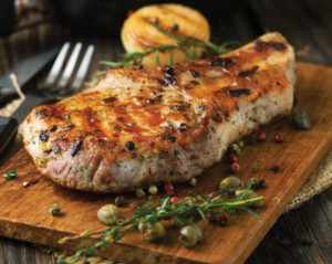 Braized pork chop with onions and herbs on a wooden cutting board