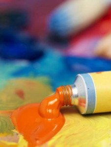 Orange oil paint squeezed out of tube with blue, yellow, red and gold around it