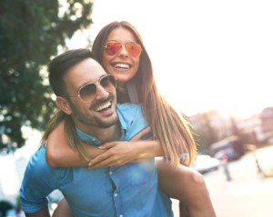 Smiling boyfriend carrying girlfriend piggyback, both wearing sunglasses